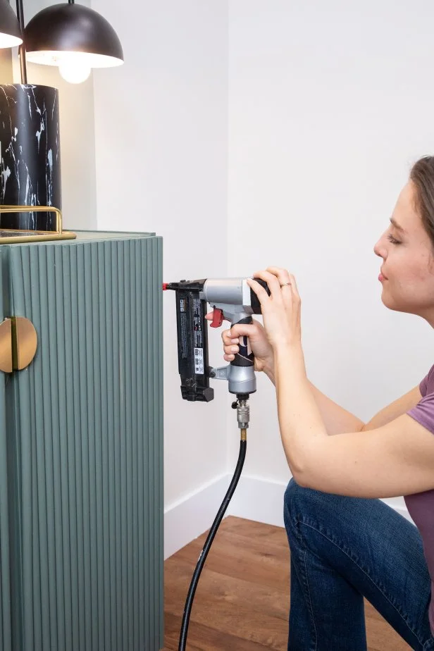 The next step in this DIY bold bar project is to add half-round dowels to the outside of the cabinets using a pneumatic brad nailer.
